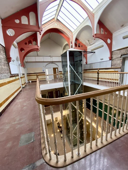 This is gallery and light-well within architect Thomas Lennox Watson’s former Adelphi Street School, a Glasgow School Board building which is being repurposed as flexible ‘found’ office space. The bright red arched roof trusses add a post modern note as the the glass lift - an intervention to improve accessibility when the school was part of the Glasgow City College campus.