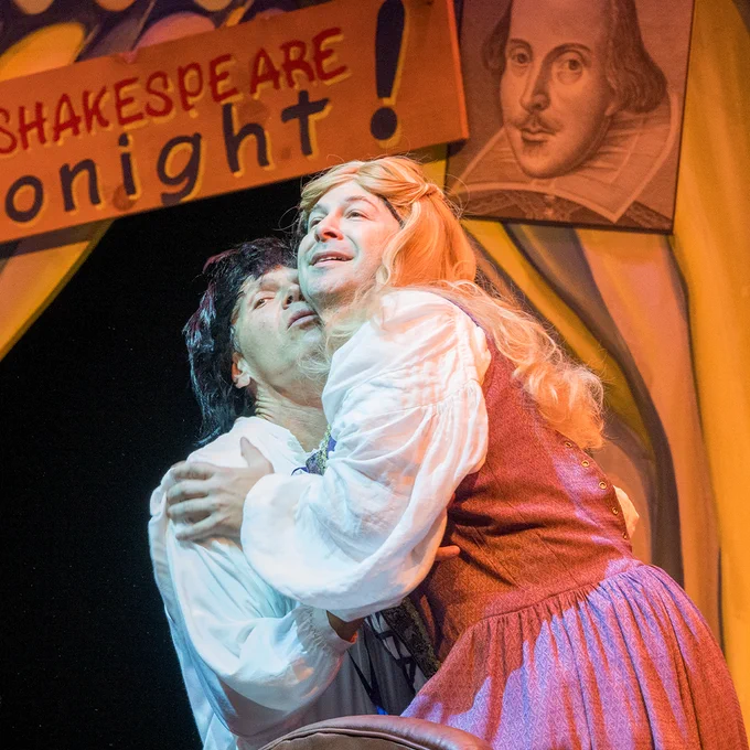 A man dressed as Romeo holds a man dressed as Juliet romantically.