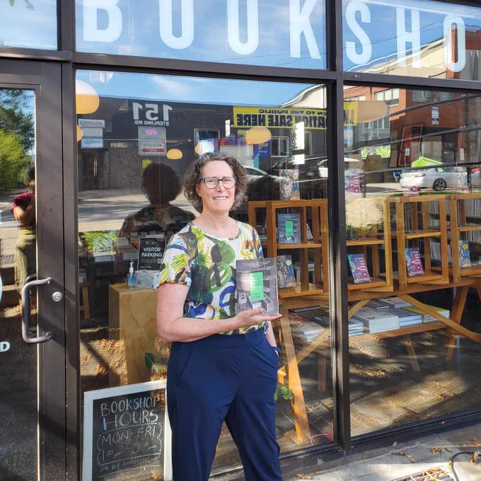 A photo of Kate Camp outside our office with How to Be Happy Though Human. 
