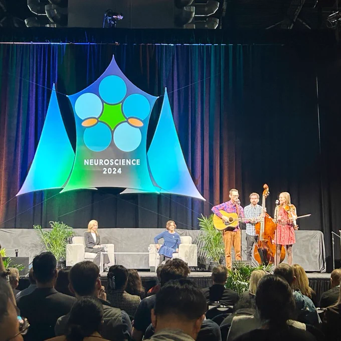 People on stage having a conversation and playing stringed instruments