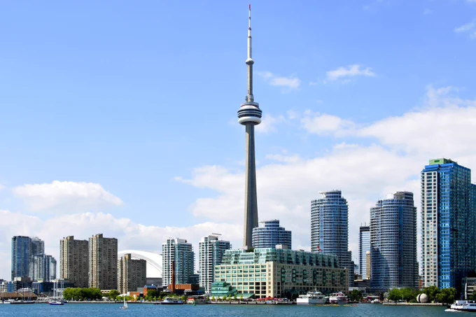 View of the Toronto skyline featuring the CN Tower, surrounded by modern buildings under a blue sky with scattered clouds.