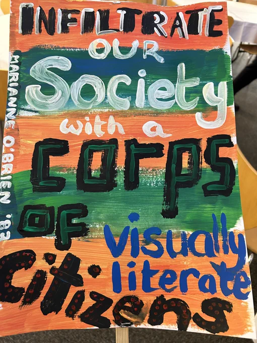 A colourful placard with a painted slogan reads ‘infiltrate our society with a corps of visually literate citizens. Marianne O’Brien ‘83’.