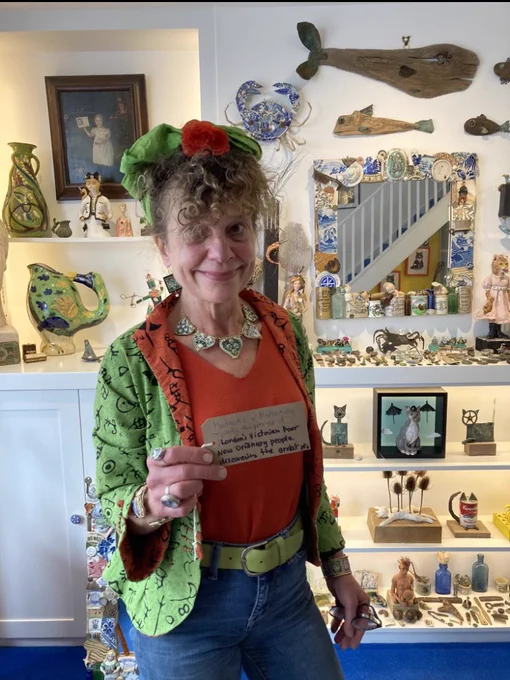 Artist Madeleine Marsh holds her note in front of@a wall of artwork