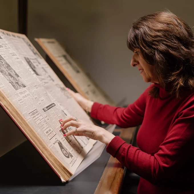 A woman consults a large format newspaper on a stand in a Reading Room at the British Library.