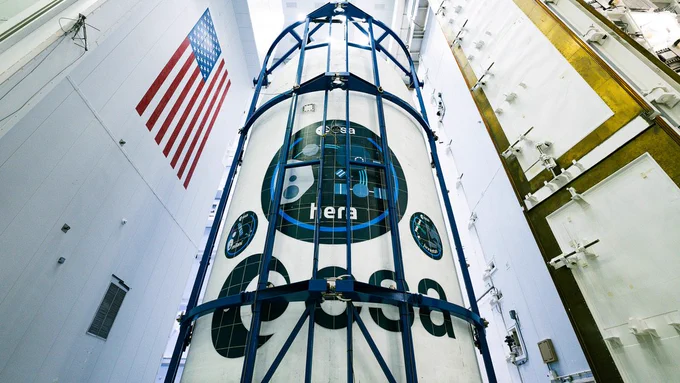 A photo of a rocketship container branded with the European Space Agency and Hera mission logos in a storage room
