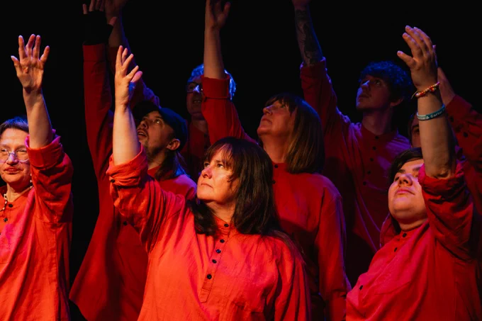 A group of actors reaching upwards with one arm, looking up.