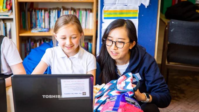 A young person working on a laptop, accompanied by an adult mentor.