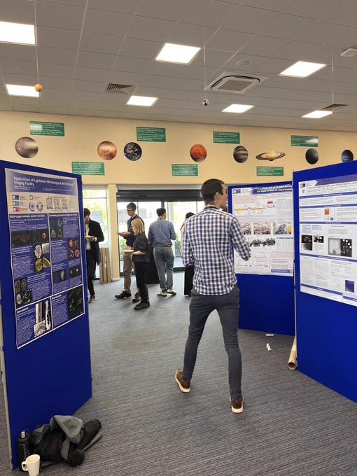 poster session: people milling around large blue poster boards with A0 conference posters on them.