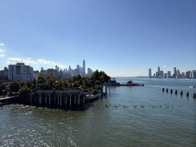 Little island, lower Manhattan, Jersey City, and the Hudson River seen from the rooftop of Pier 57. Bright blue sky with minimal cloud coverage.