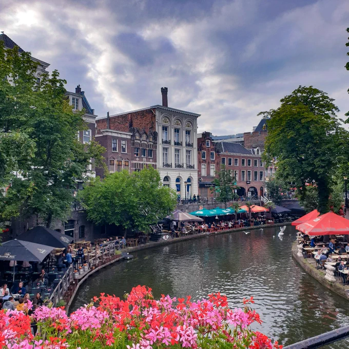 A canal in Utrecth, closest to the water is packed with resturants and above them the house facades are clearly seen between trees. Photo by Jonne Mäkikyrö on Unsplash
