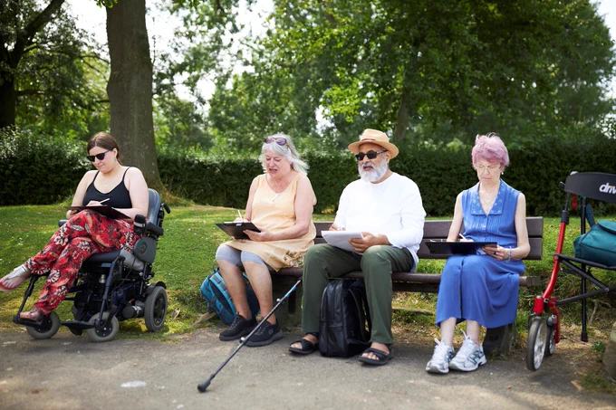 Four people sat in a park drawing the scenery around them. 