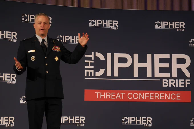 A man in a US Air Force uniform stands on stage gesturing as he speaks. The wall behind him reads "The Cipher Brief Threat Conference."