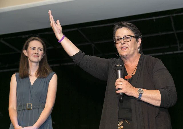 Mari is holding a microphone with her other hand raised addressing the crowd at the Dublin Honours Magdalenes event. Maeve O'Rourke is looking on with admiration. Photo credit: Paul Sherwood.