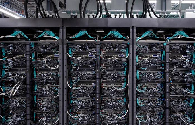 Side view of the supercomputer Frontier with its cabinets open to show masses of teal and white wires connecting together computing cores