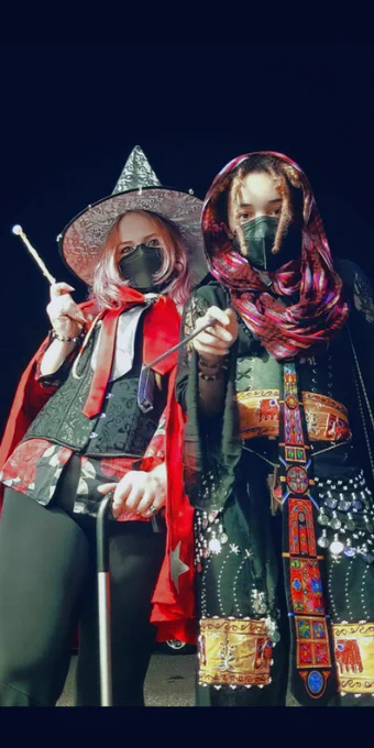 ID: selfie of Jules and Kei, a non-binary lesbian couple, dressed as wizards. They are visible from the knees up, photographed from a low angle