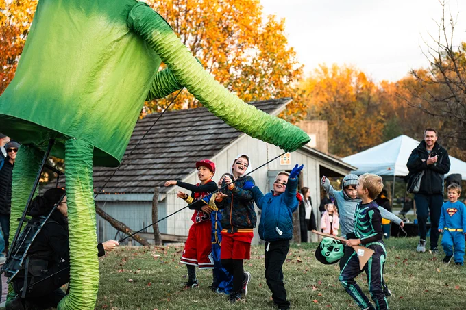 Children in Halloween costumes play with larger than life puppet