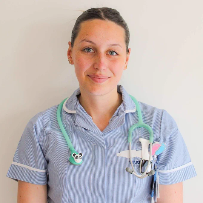 Katie is smiling and standing in her student uniform. She has a light green stethoscope around her neck that has a small panda face on it.