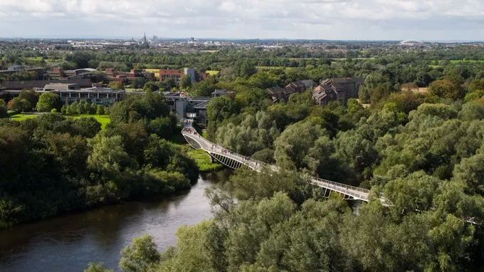 Photograph of a long, curved pedestrian bridge over a wide river lined by dense trees