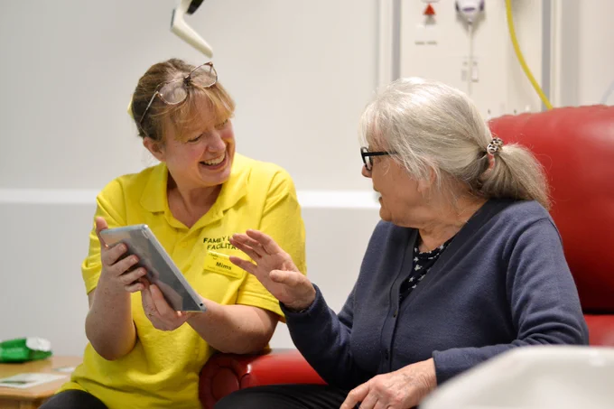 A member of staff speaks to a patient while holding a tablet computer.