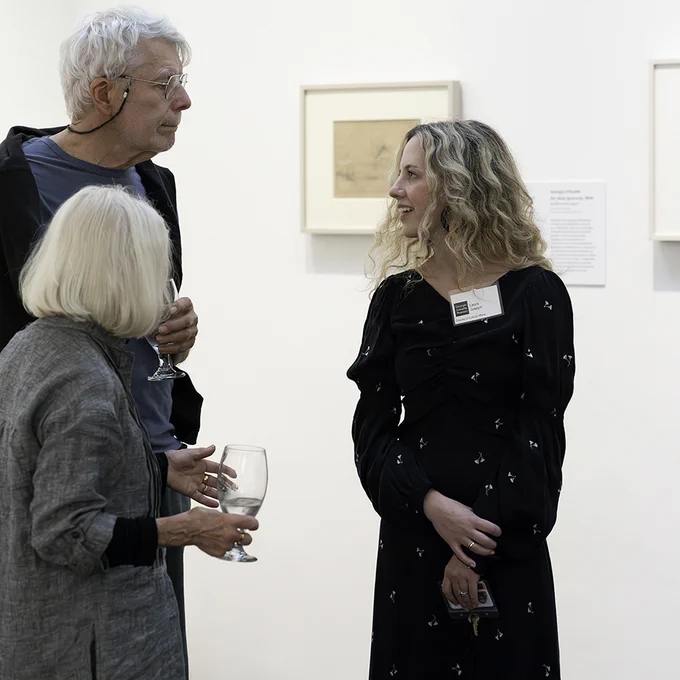 Photograph of two people talking animatedly with a third person in a gallery.