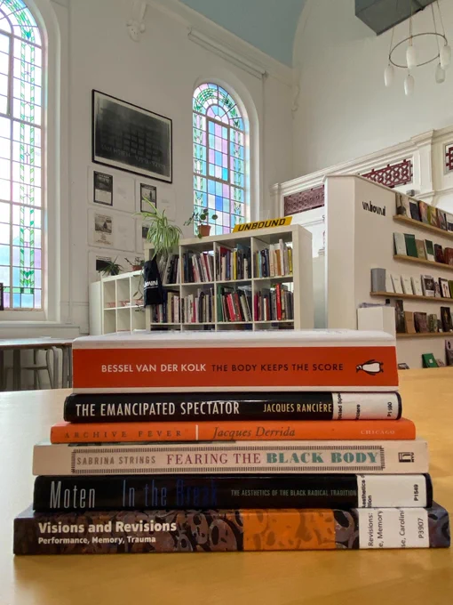 Pile of books on a desk, in an office space. The books are:

Visions and Revisions: Performance, Memory, Trauma - Bryoni Trezise, Caroline Wake

Archive Fever - Jacques Derrida

The Emancipated Spectator  - Jacques Rancière

The Body Keeps the Score - Bessel Van Der Kolk 

Fearing the Black Body: The Racial Origins of Fat Phobia - Sabrina Strings 