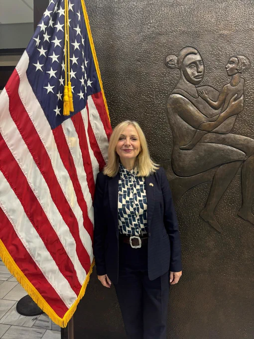 The Mayor of West Yorkshire, Tracy Brabin, is stood in front of an American flag. She is smiling to camera. 