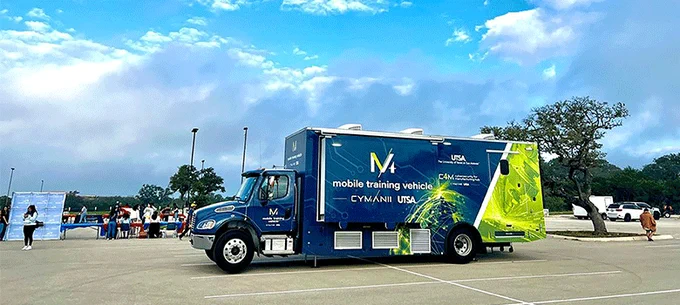 A mobile training vehicle from UTSA parked in a spacious outdoor area with people milling around.