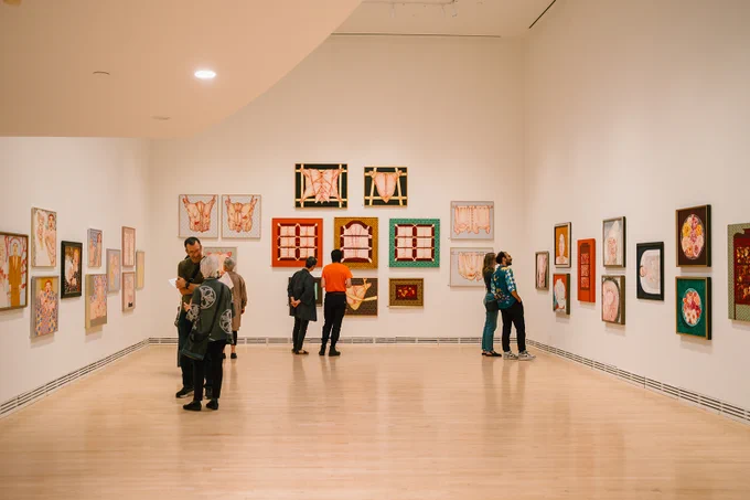 Visitors viewing colorful artwork at a gallery exhibition.