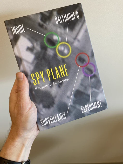 Photo of hand holding book titled Spy Plane: Inside Baltimore's Surveillance Experiment