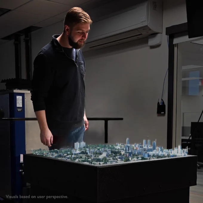 In a visual illustration, a man looks at a 3D-image of a city rising up from a table.