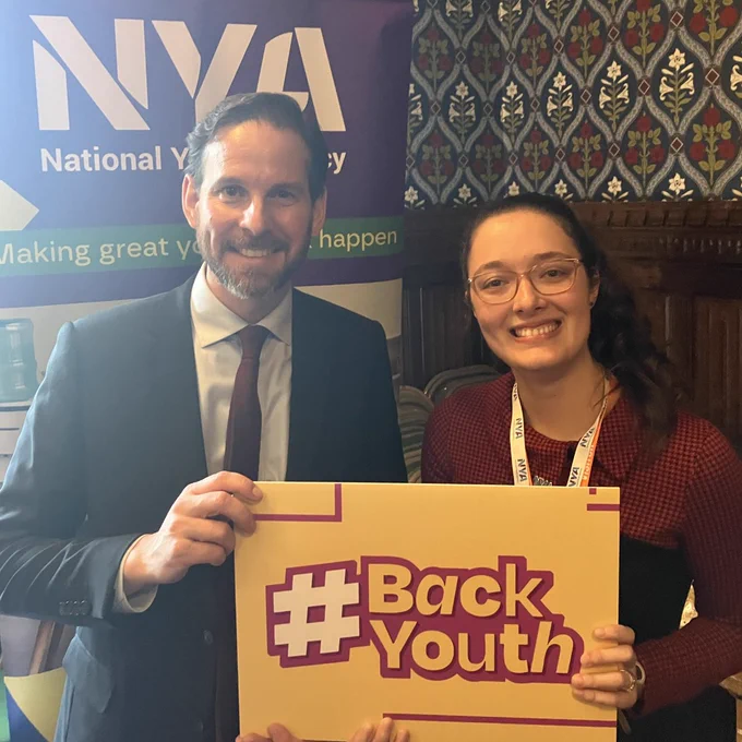 A photo of NYA Policy and Public Affairs Manager, Angel with MP Alex Ballinger. They hold up a sign with the hashtag #BackYouth
