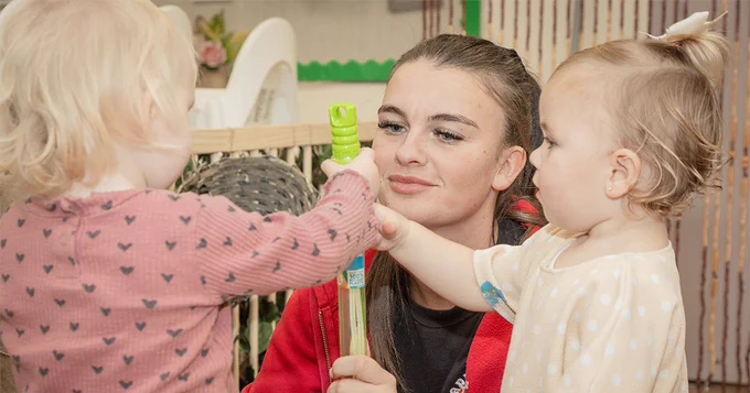an early years working is helping two young children within a nursery.