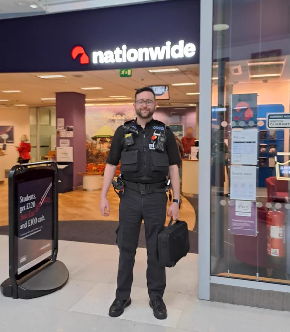 A picture of PC Wilcox in uniform standing outside of Nationwide Bank in Kingfisher Station