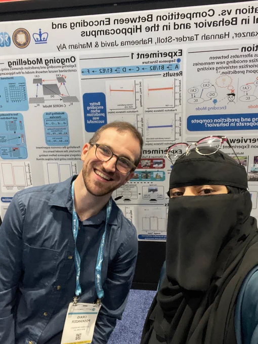 A tired Raheema and Craig smiling in front of their poster 