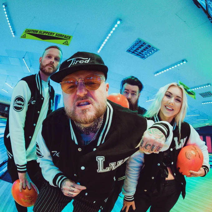 Four people at a bowling alley. Man at the front of the four wearing sunglasses with his fist clenched, facing the camera.