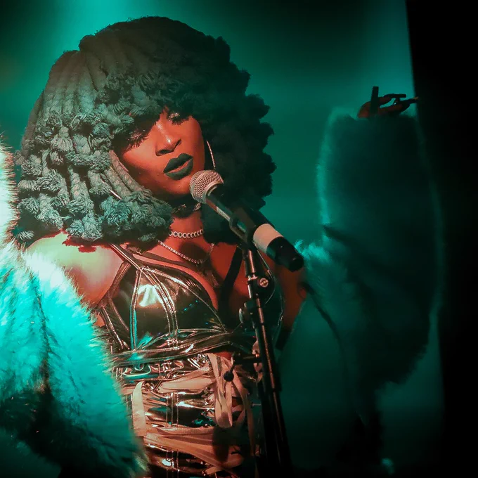 Lady with eyes closed behind microphone, arm in the air.