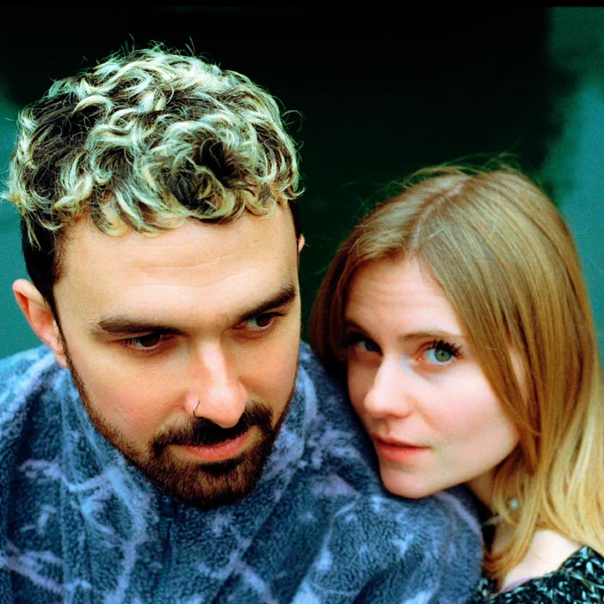 Close up of man with beard and short hair and women looking towards the camera.