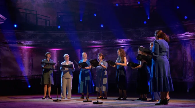 A small choir of female singers in a dramatically lit hall
