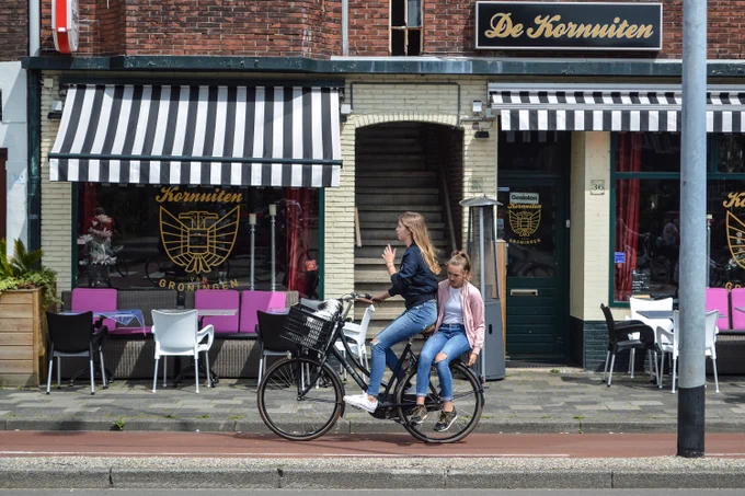 Two teens cycling in Groningen. One of home sits on the back.