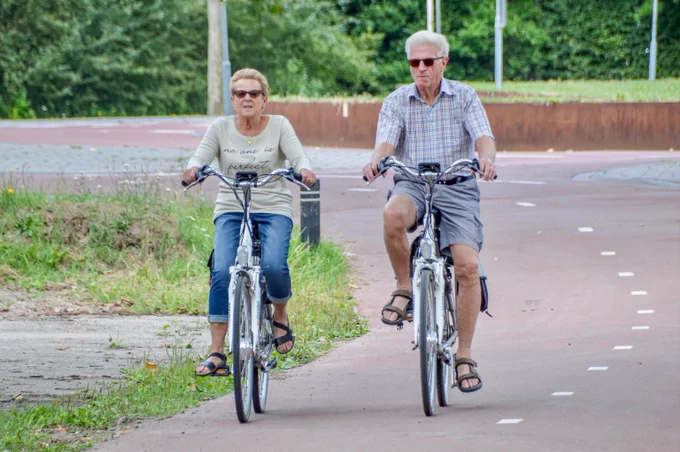 Two seniors cycling towards the camera on a cycling path