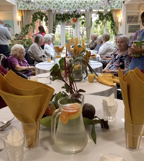 Group of older people , seated around a table which has fruit and vegetable centrepieces and bright yellow napkins