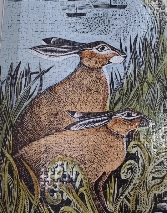 A picture of a completed jigsaw, showing a drawing two hares on a riverbank with ferns and grasses, with water and small boats in the background.