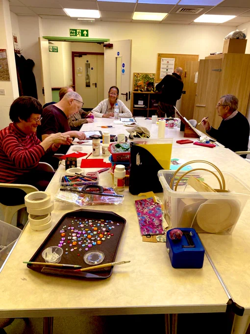 A group of people sitting around a table with art materials spread out across it. Everyone looking like they are concentrating very hard.