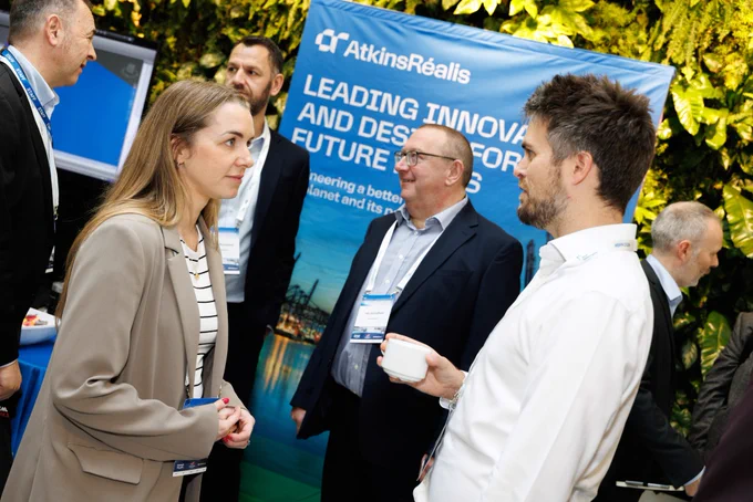A group of delegates network over tea and coffee, in front of an exhibition stand from AtkinsRealis