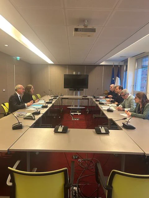 Photographie de la réunion entre le ministre, le collectif Alerte et la délégation interministérielle. Tous les participants sont assis autour d'une table et échangent entre eux.