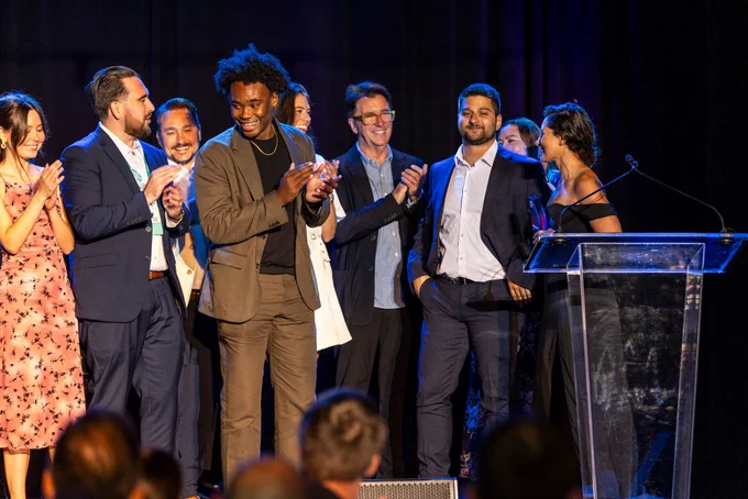 Group of individuals applauding on stage at an awards ceremony with one person standing at a podium.