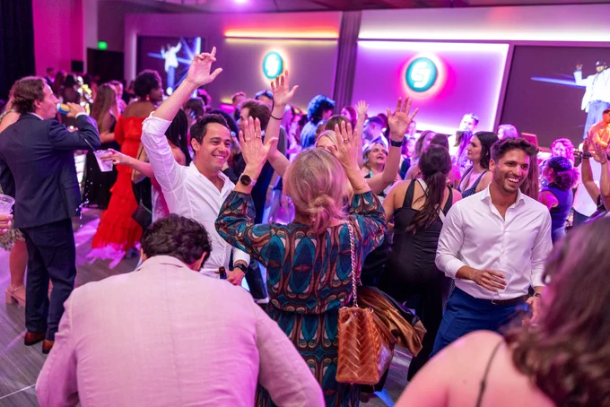 Several people enthusiastically dancing and celebrating at a lively event with vibrant lighting.