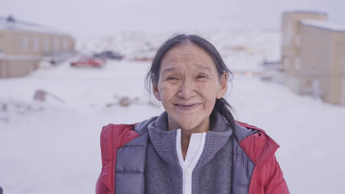 Shuvinai Ashoona’s portrait has her smiling against a snowy backdrop in a red winter parka.