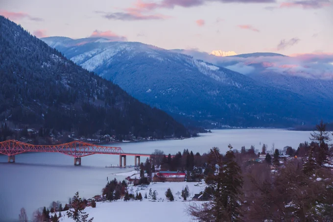 A bridge over a lake with snow and mountains in the background.