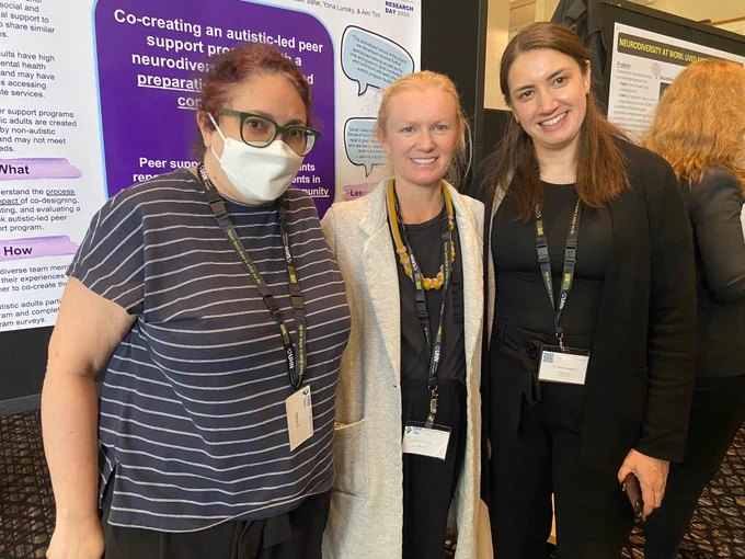3 women smiling and standing next to poster